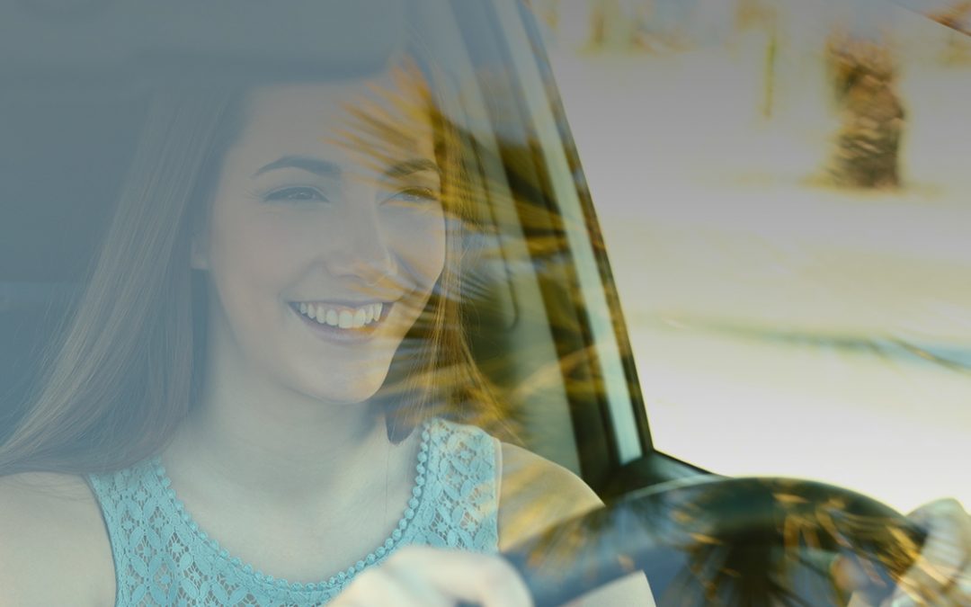 A smiling young female driver behind the wheel of a car.