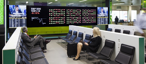A man and a woman sit watching the stocks on a digital screen in the Bloomberg London City Airport lounge.