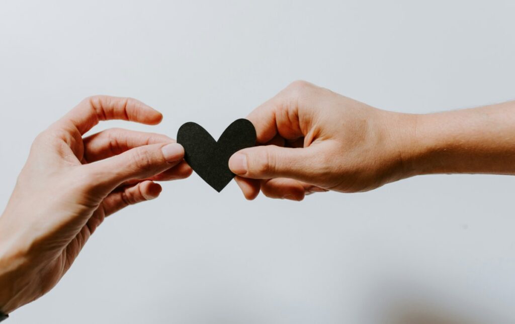 Two hands holding a black paper heart between them.